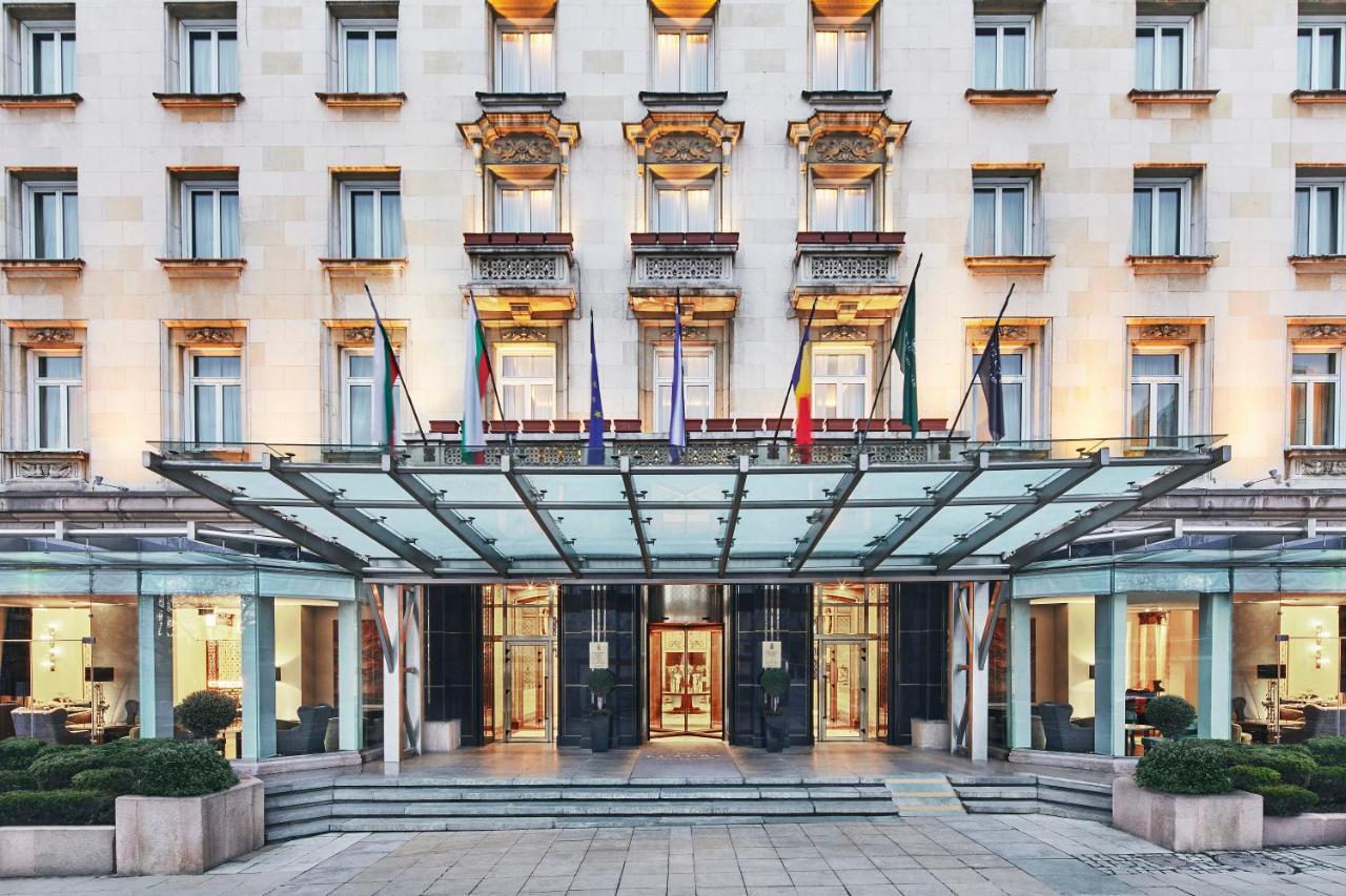 Sofia Balkan Palace Esterno foto The photo shows the exterior of a luxury hotel. The building features a classic architectural style with a light-colored facade, adorned with decorative elements such as balconies and window frames. Above the entrance, there is a stylish glass canopy